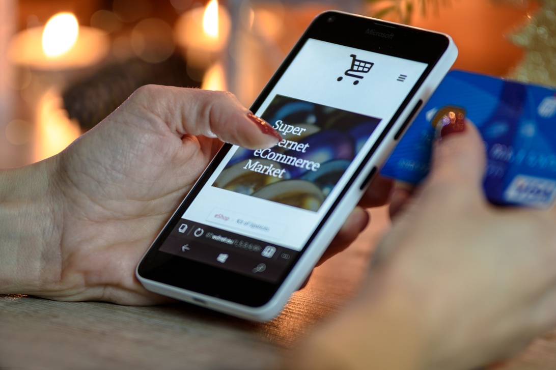 Närbild på händer som håller en smartphone med en varukorg i en e-handelsapp och ett kreditkort, vilket illustrerar mobil e-handel.